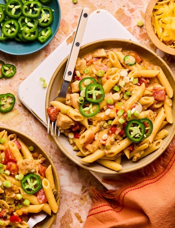 Bowl of penne pasta with cooked diced chicken, chopped bell pepper, chopped onions, creamy sauce, and topped with sliced jalapeno.