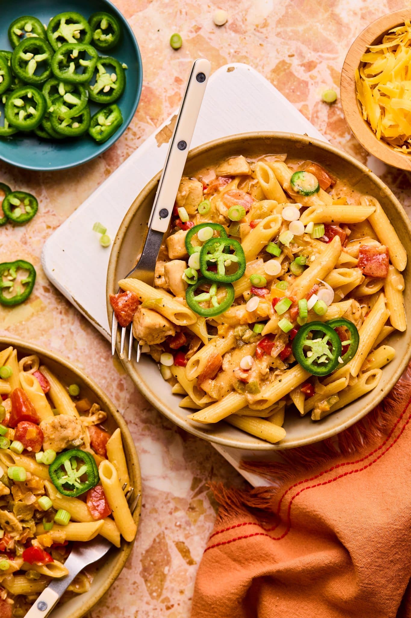 Bowl of penne pasta with cooked diced chicken, chopped bell pepper, chopped onions, creamy sauce, and topped with sliced jalapeno.