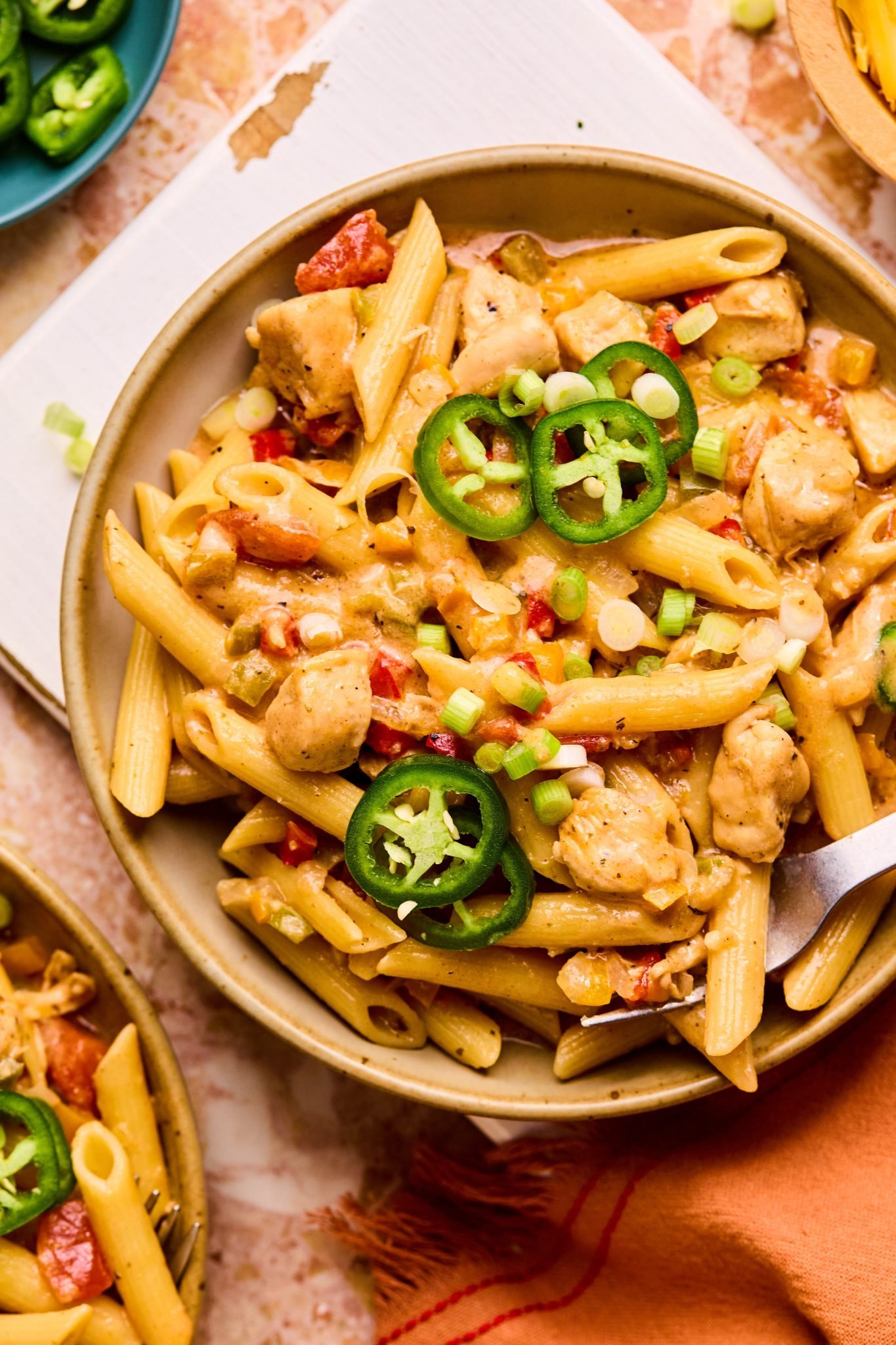 Bowl of penne pasta with diced chicken, chopped bell peppers, chopped onions, and sliced jalapenos on top.