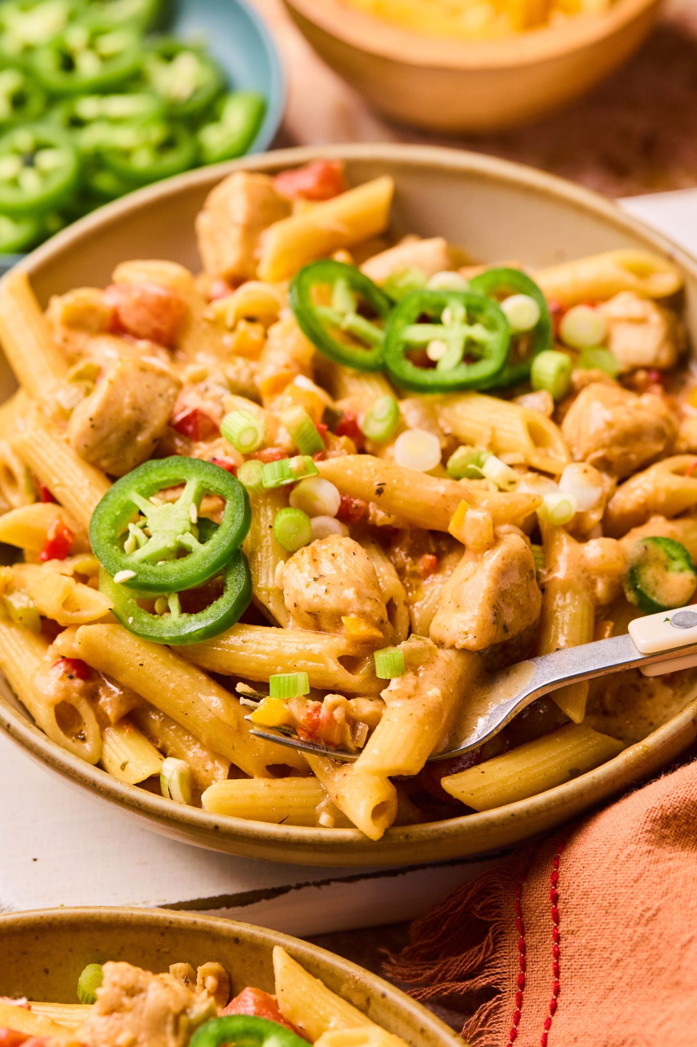 Close up image of a bowl of penne pasta with a creamy sauce, diced chicken, chopped bell peppers, chopped onions, and topped with sliced jalapeno and sliced green onions.