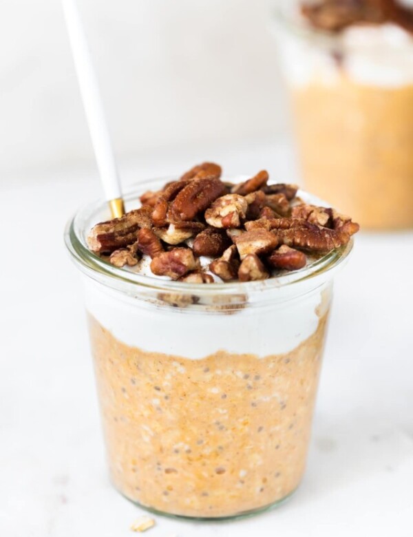 overnight oats made with pumpkin puree in a glass jar topped with Greek yogurt, chopped pecans and ground cinnamon