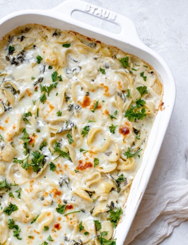 baked pasta with spinach and artichokes covered in cheese and parsley