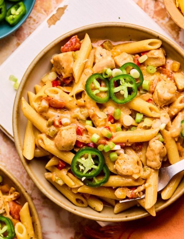 Bowl of penne pasta with diced chicken, chopped bell peppers, chopped onions, and sliced jalapenos on top.