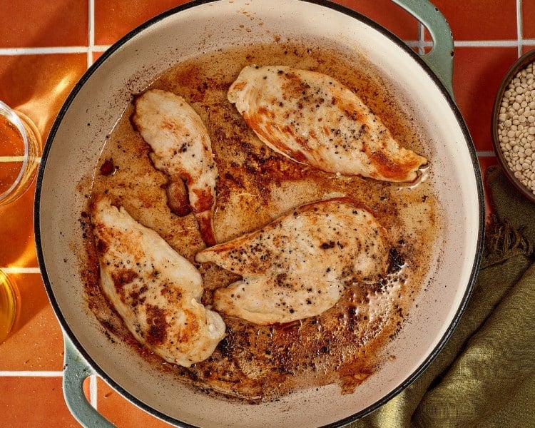Seasoned chicken breasts searing in a large skillet until golden brown on both sides.