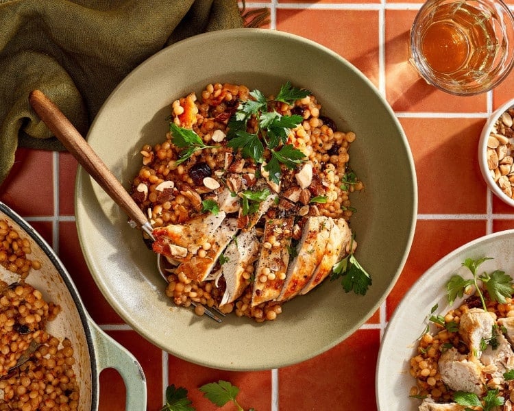 Cranberry apricot chicken and pearl couscous served in a bowl with chopped almonds, fresh parsley, and sliced golden-brown chicken.