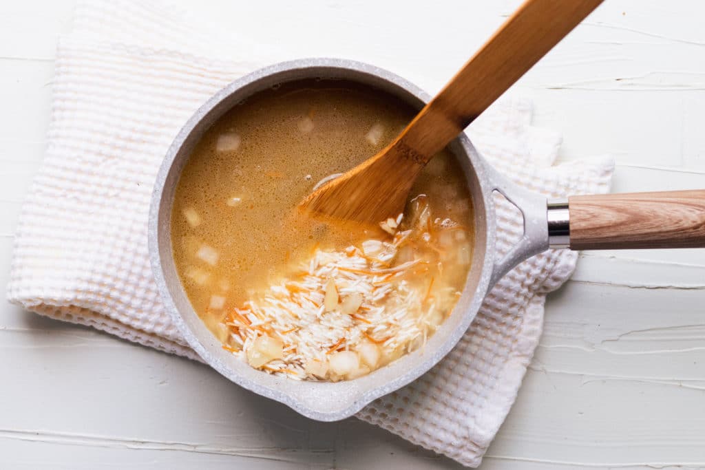 rice and broth in a saucepan with a wooden spoon