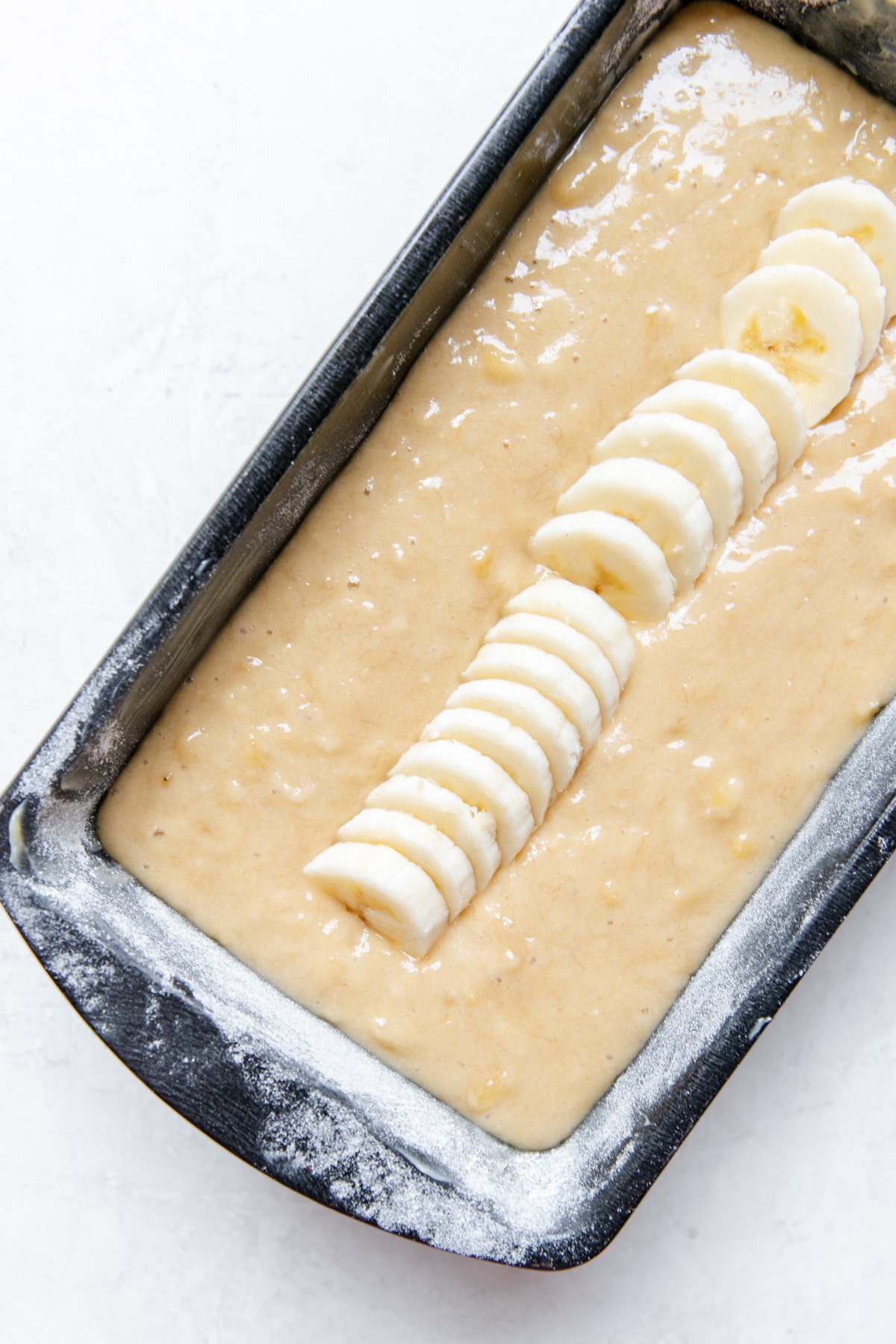 batter for a banana bread in a 9x5 inch baking pan topped with sliced bananas