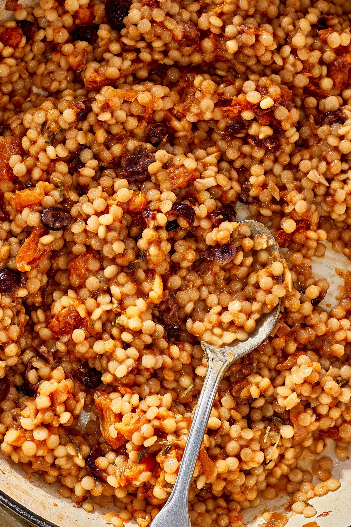 Close-up of pearl couscous cooked with dried cranberries, chopped apricots, herbs, and a savory-sweet sauce.