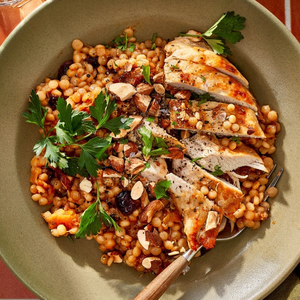 Sliced cranberry apricot chicken served over pearl couscous with dried cranberries, apricots, chopped almonds, and fresh parsley.