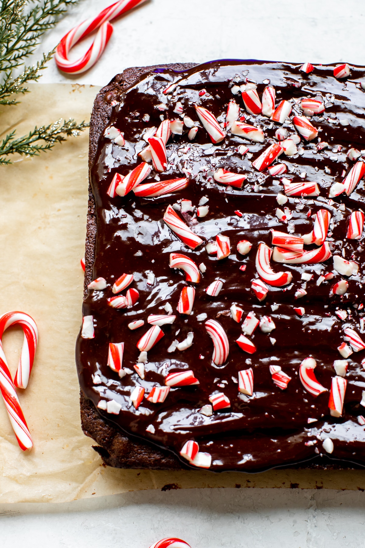 brownies on parchment paper topped with ganache and chopped candy canes