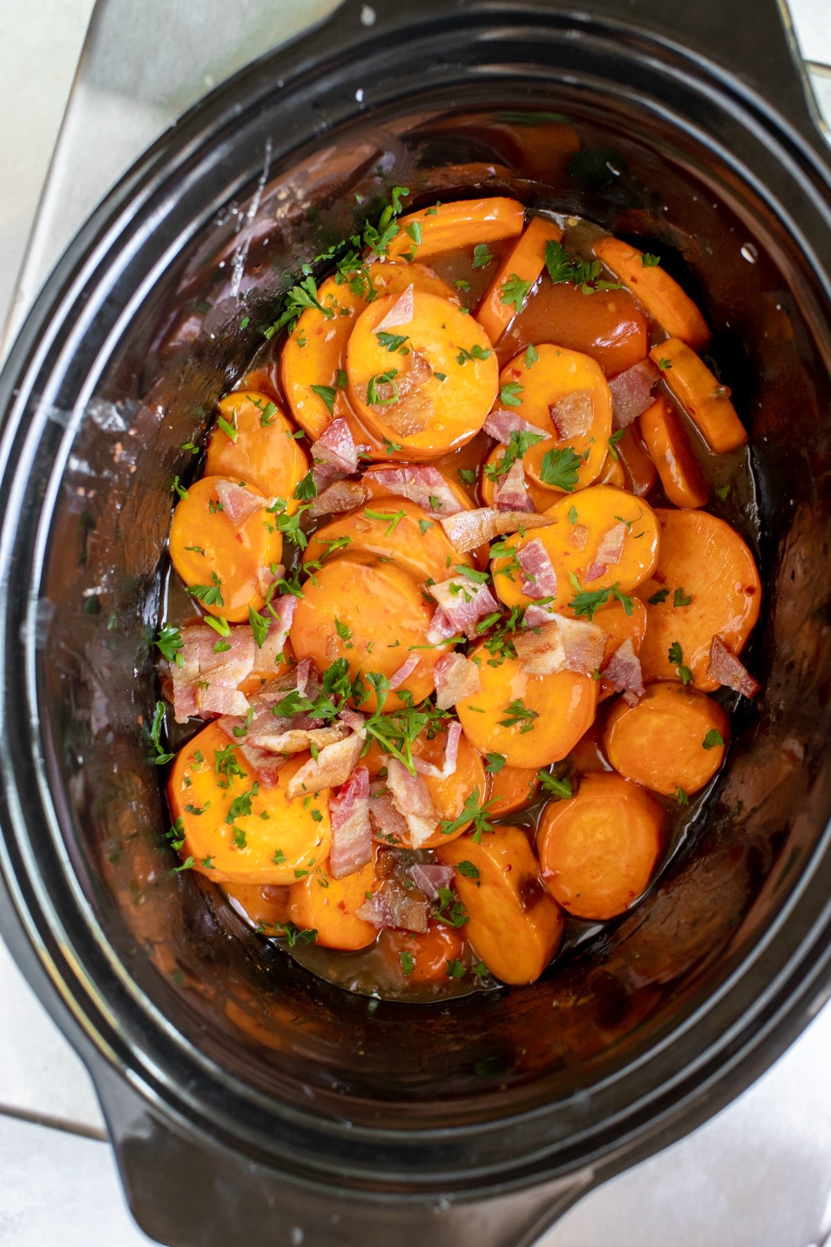 sweet potatoes sliced into rounds, in a black crock pot topped with bacon crumbles and parsley