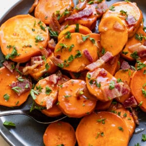 sweet potatoes on a blue plate topped with honey, bacon and parsley
