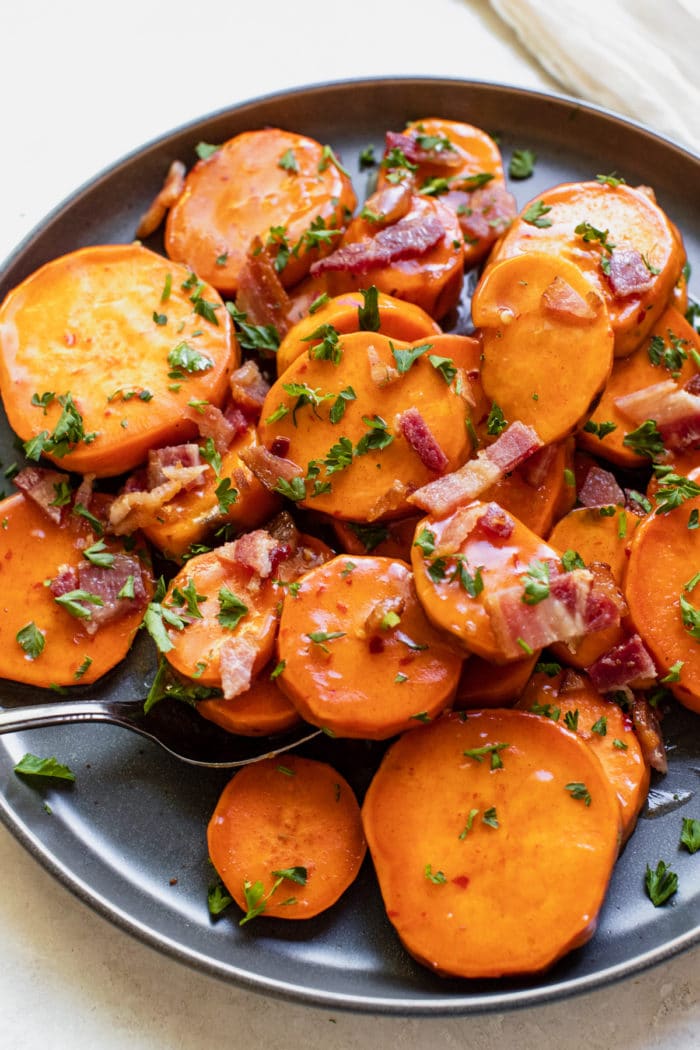 sweet potatoes on a blue plate topped with honey, bacon and parsley