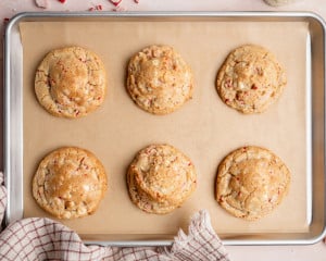 Six freshly baked white chocolate peppermint cookies cooling on a parchment-lined baking sheet.