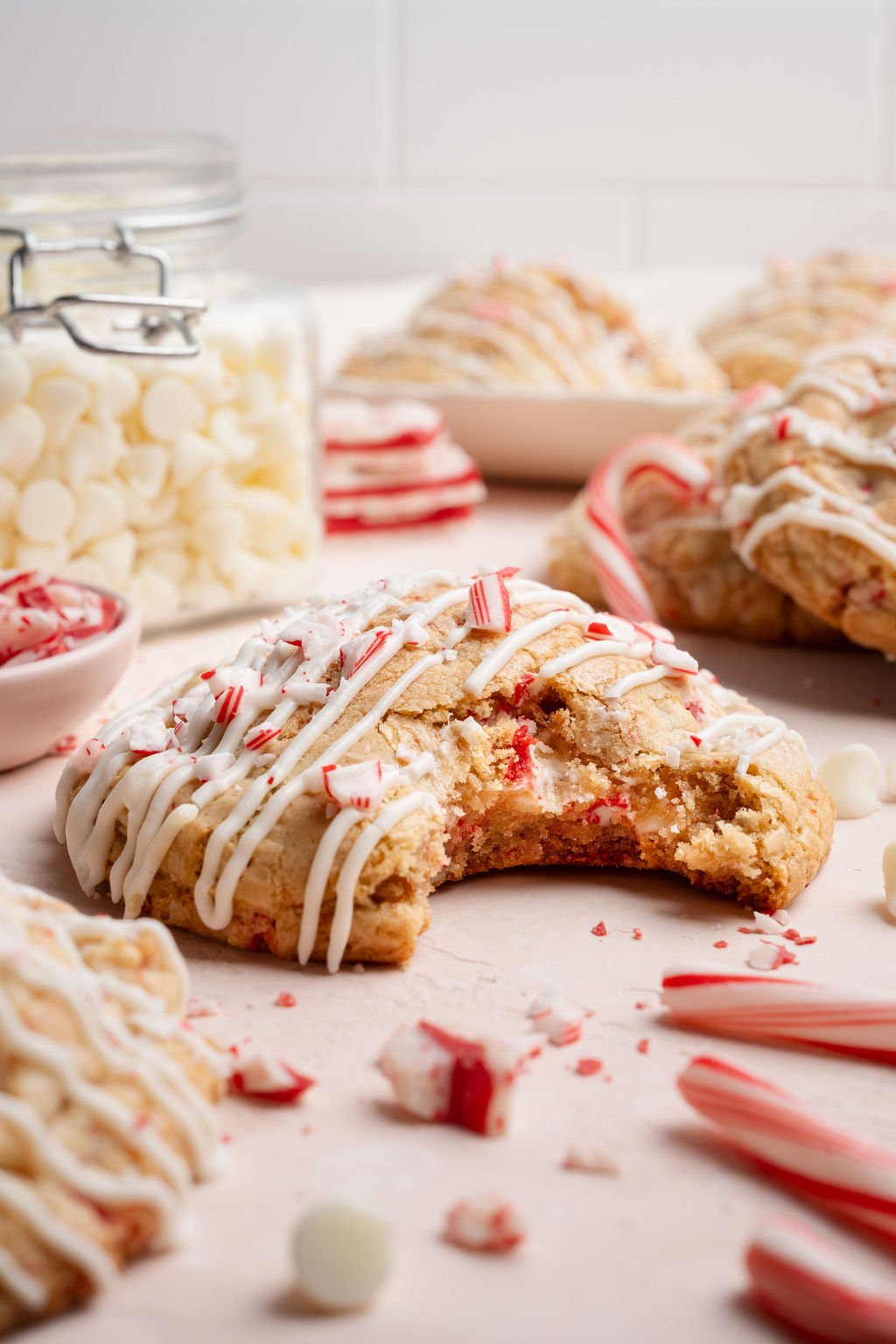 Close-up of a white chocolate peppermint cookie with a large bite taken out, showing the soft, chewy interior studded with white chocolate chips and peppermint pieces.
