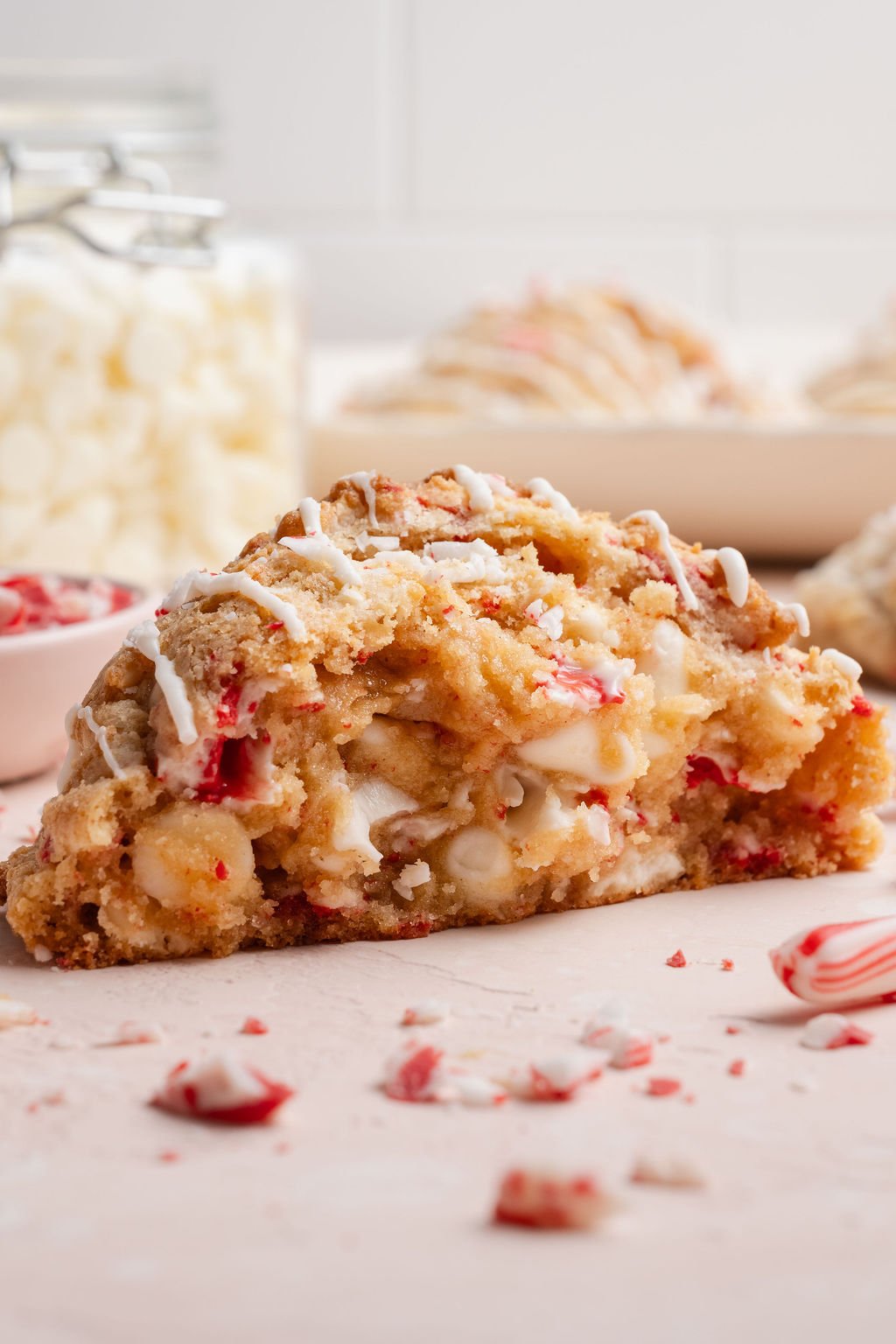 Side view of a thick, chewy white chocolate peppermint cookie broken in half to show the melty white chocolate and peppermint pieces inside.