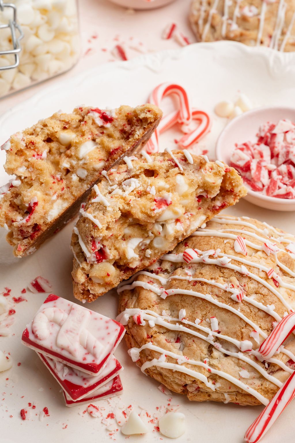 White chocolate peppermint cookies on a plate with a stacked peppermint bark square, candy canes, and crushed peppermint scattered around.