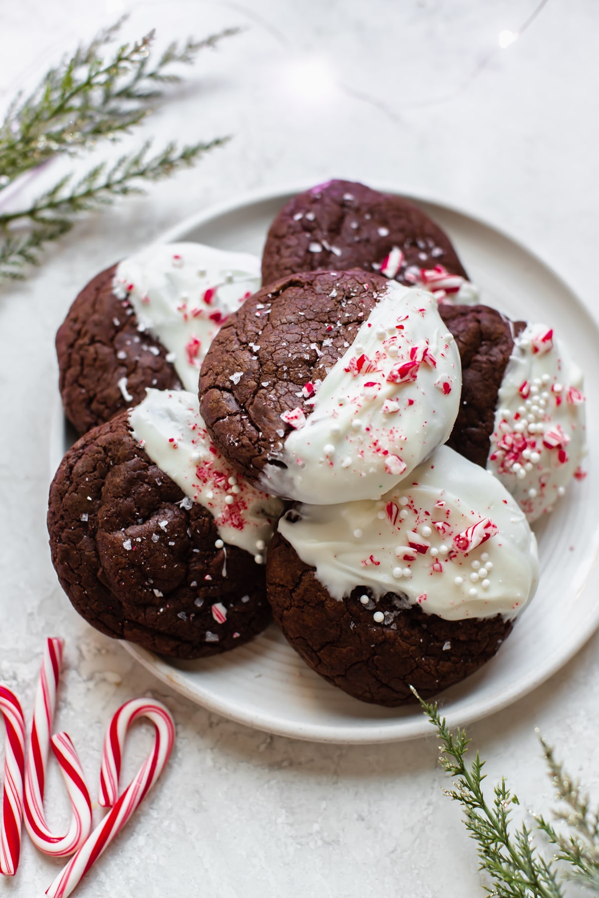 a stack of chocolate cookies dipped in white chocolate and garnished with crushed candy canes on a white plate