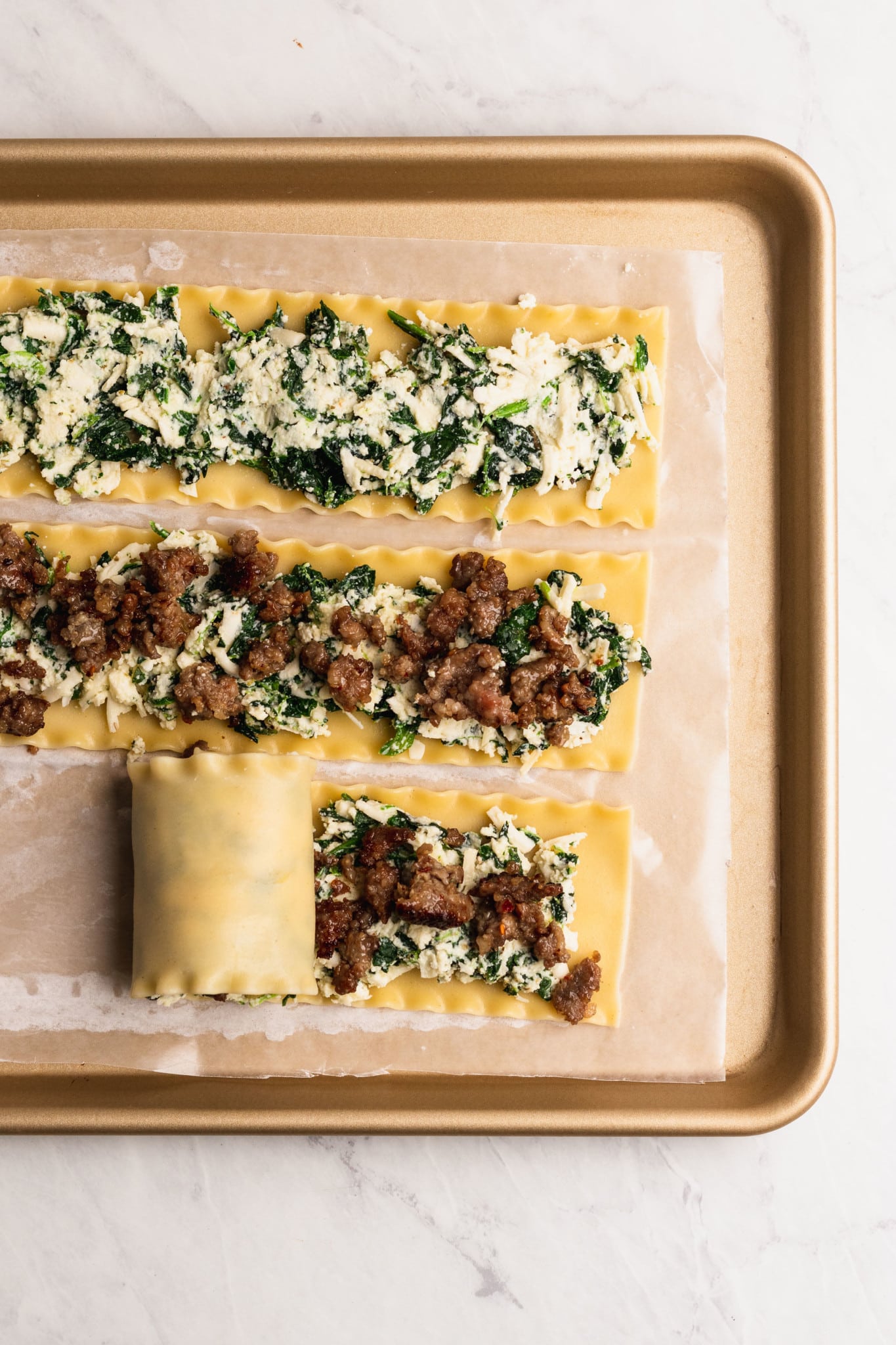 cheesy spinach ricotta with italian sausage rolled up into a lasagna noodle on a baking sheet