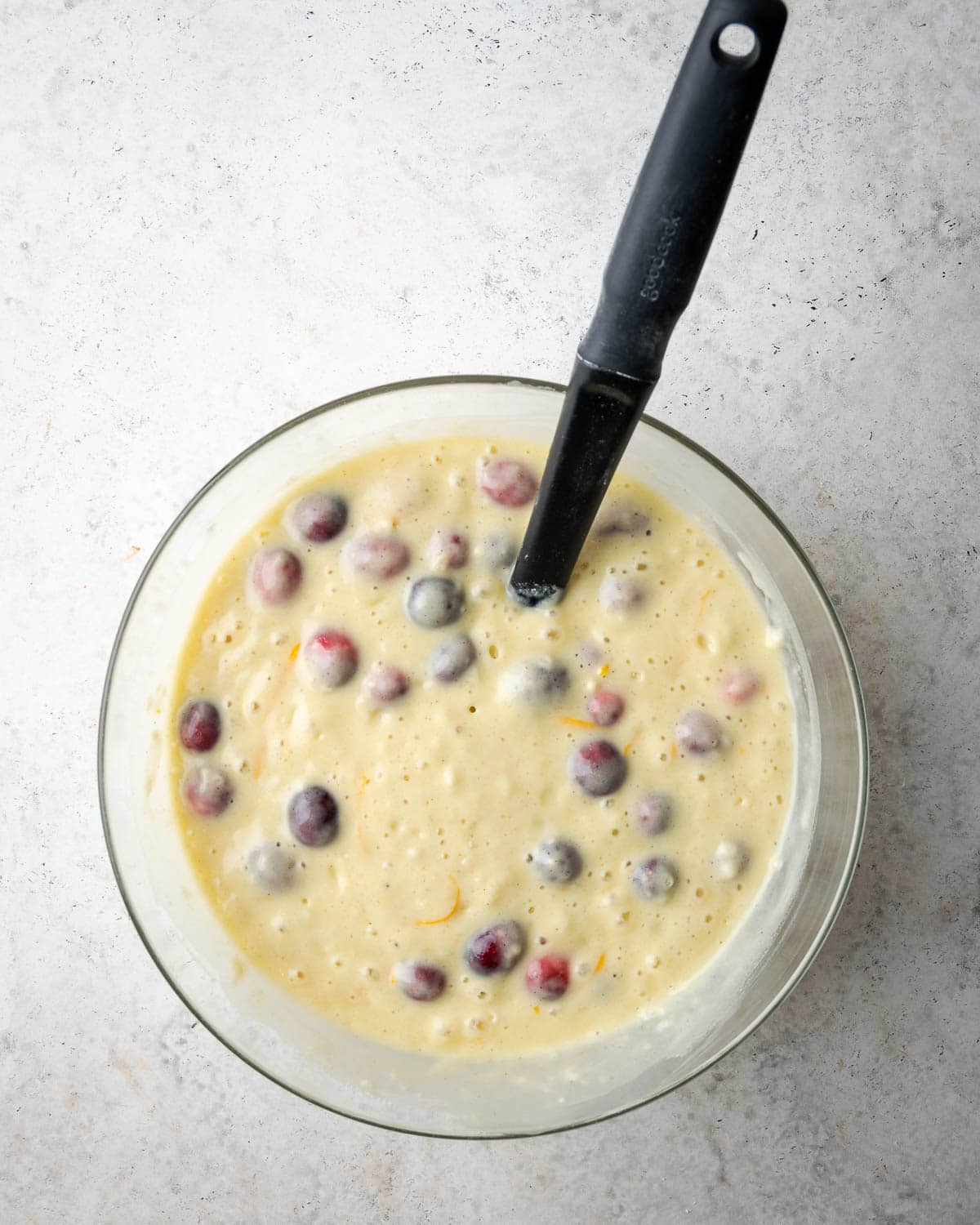 bread batter in a glass bowl with orange zest and cranberries folded in