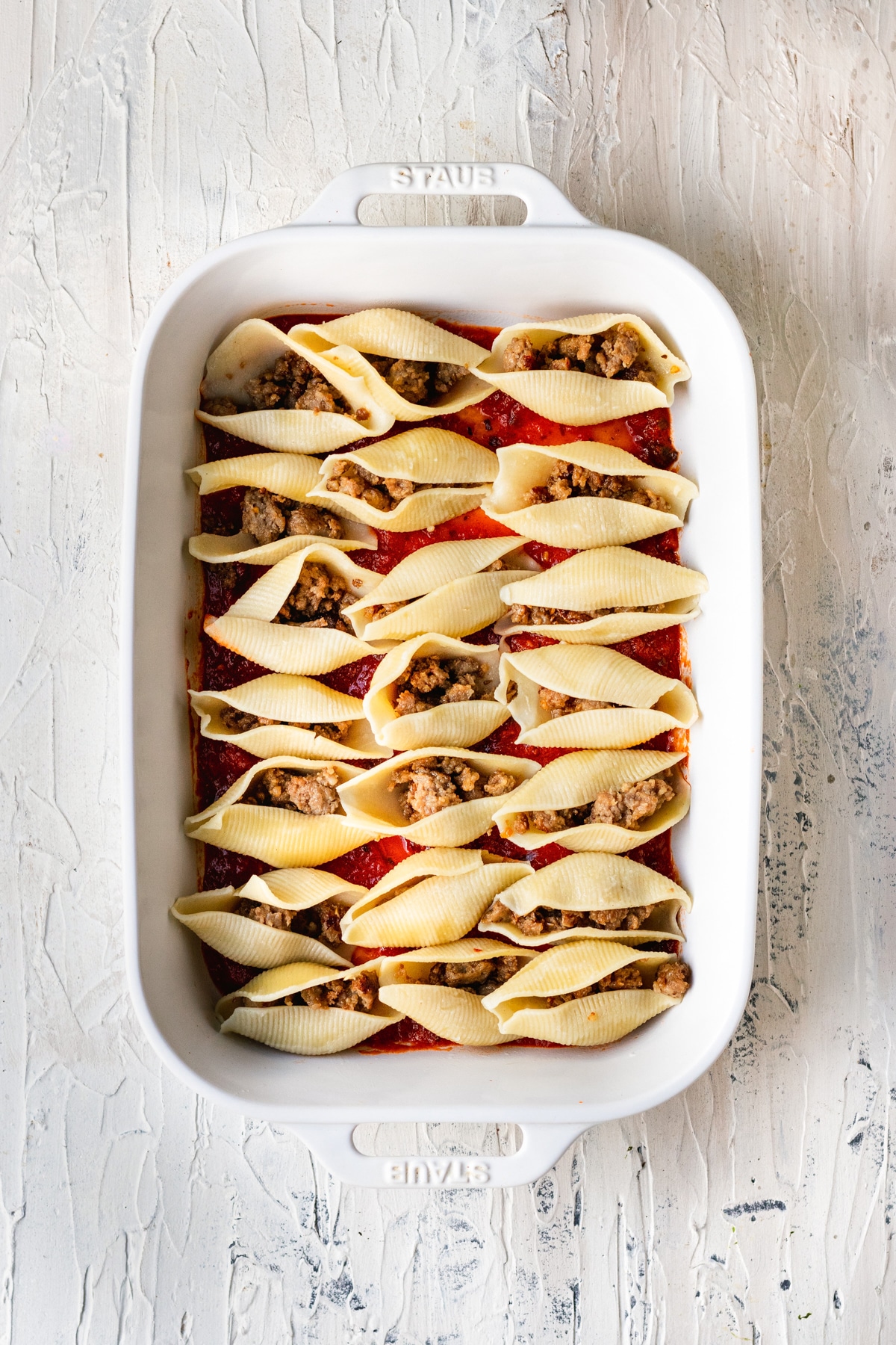 shell pasta in a casserole dish filled with ground italian sausage