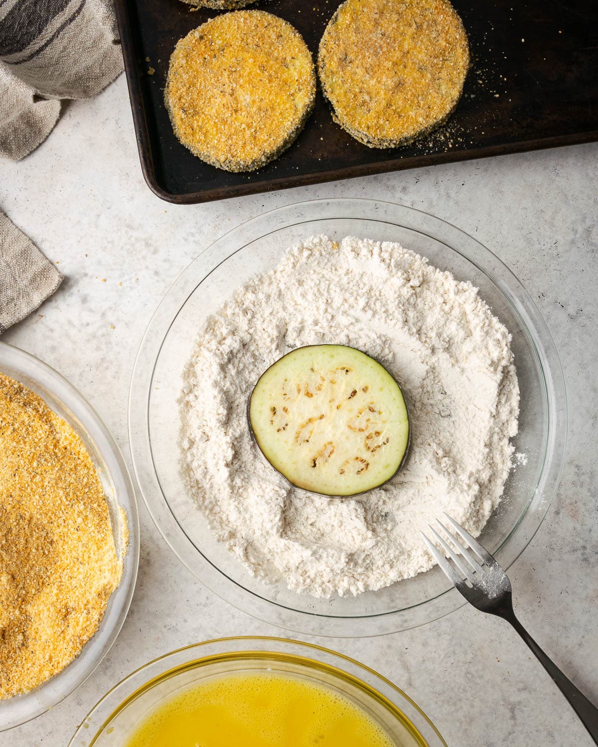 dredging eggplant in flour in a glass bowl