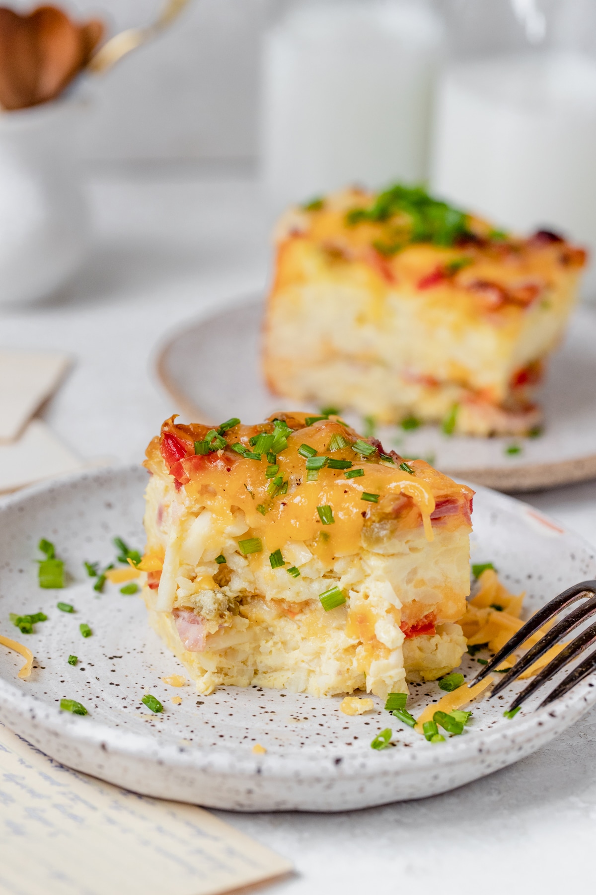 a slice of breakfast casserole on a white speckled plate with chives on top