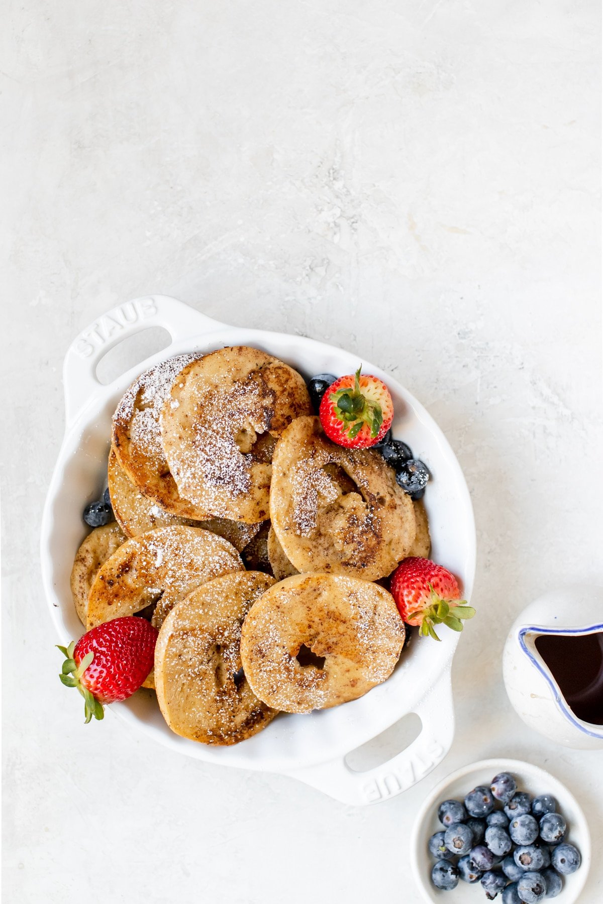 bagels in a white dish with fresh berries, syrup and powdered sugar on top