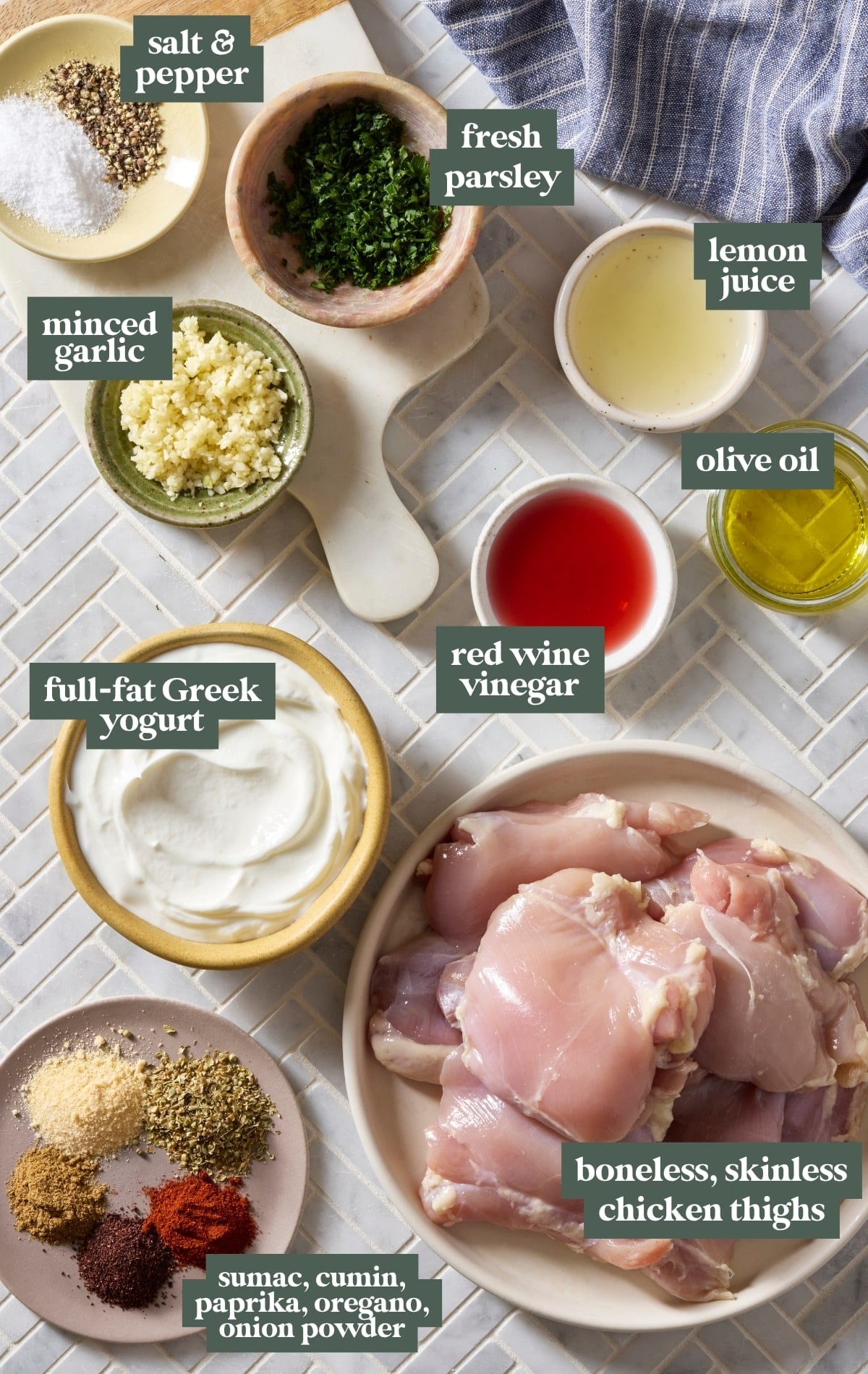 Ingredient shot for Greek yogurt lemon chicken featuring boneless skinless chicken thighs, full-fat Greek yogurt, olive oil, lemon juice, red wine vinegar, garlic, parsley, spices, salt, and pepper arranged on a countertop with labels.