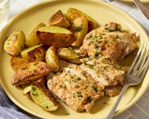 Serving of Greek yogurt lemon chicken with roasted potatoes on a yellow plate, showing sliced chicken topped with parsley and served with pan juices.