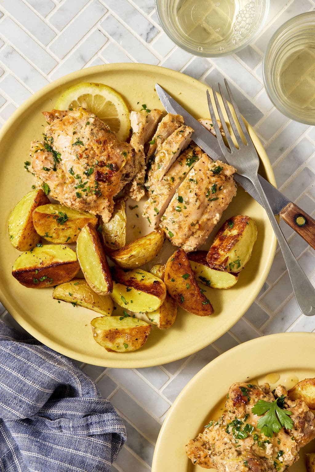Single serving of Greek yogurt lemon chicken with roasted potatoes on a yellow plate, garnished with parsley and a lemon slice, with sliced chicken showing its juicy interior.