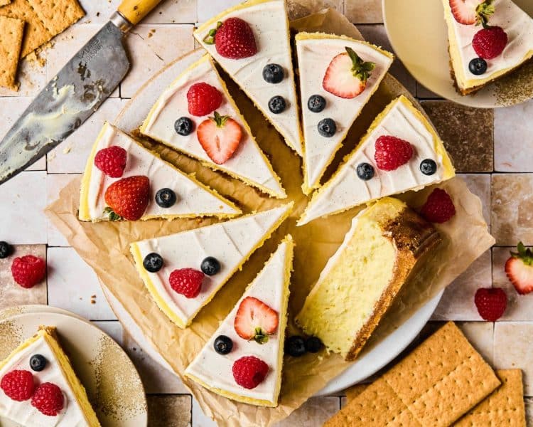 Whole circular cheesecake cut into slices and topped with berries.