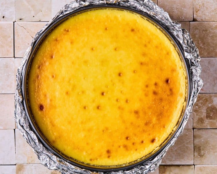 Round cheesecake in a pie pan lined with foil, after coming out of hte oven.