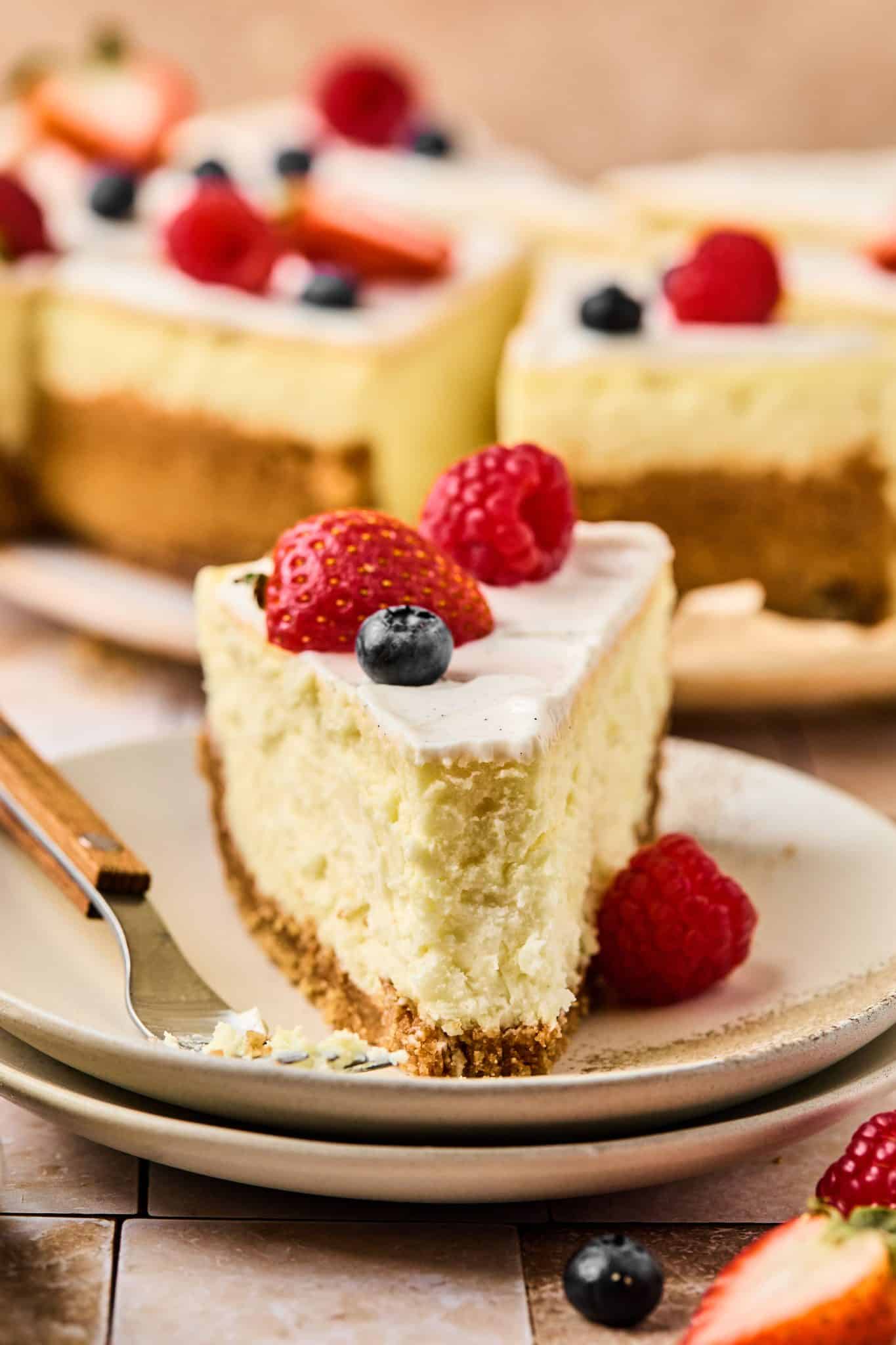 Slice of cheesecake topped with vanilla bean frosting and topped with berries on a speckled plate.