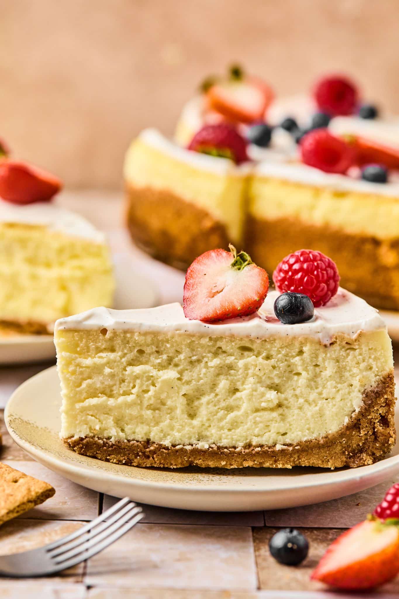 Slice of cheesecake with a graham cracker crust, vanilla bean frosting, and topped with berries.