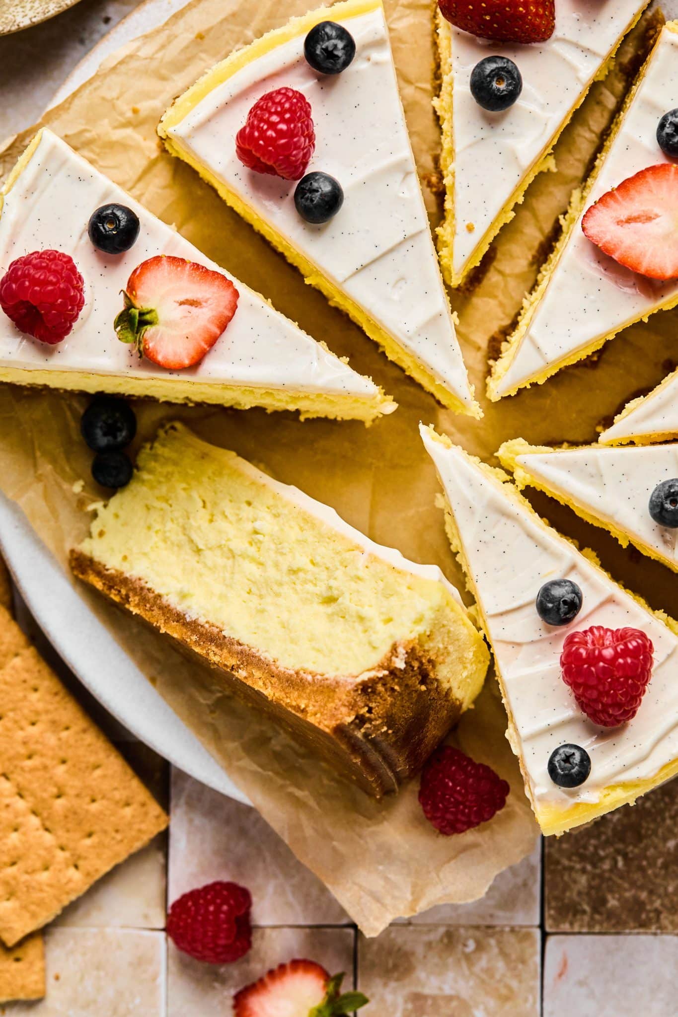 Slices of cheesecake topped with berries with one slice on its side showing the graham cracker base.