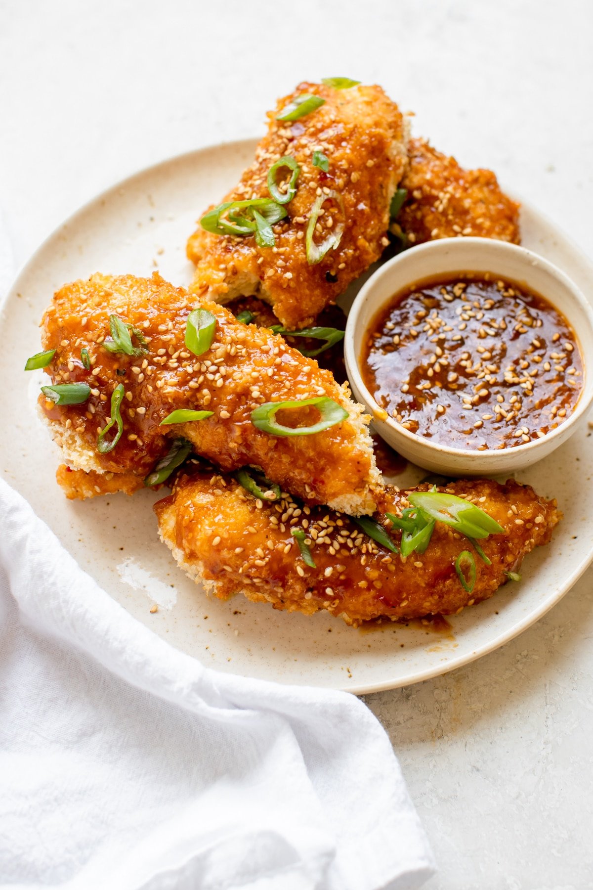 chicken tenders on a plate with sesame sauce and green onions on top