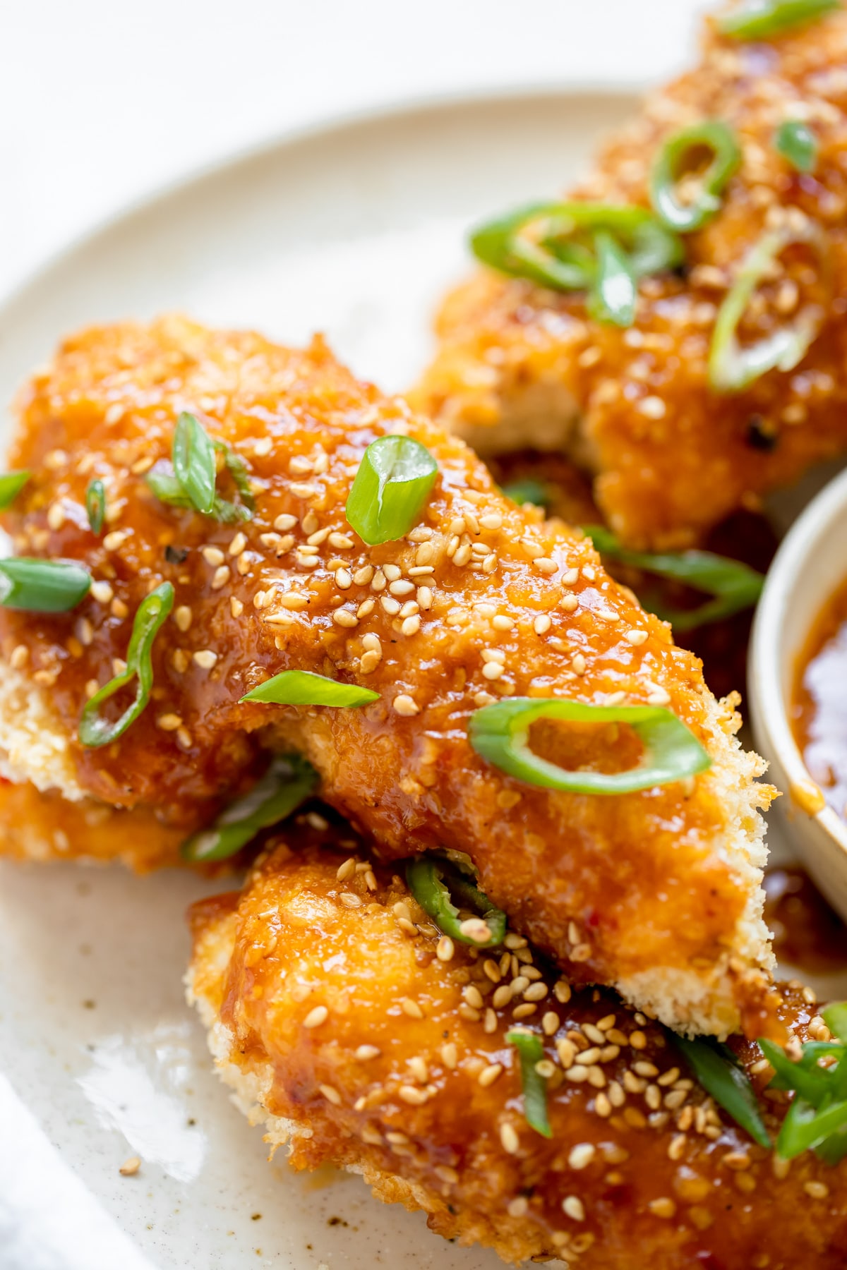 chicken tenders on a plate with sesame sauce and green onions on top