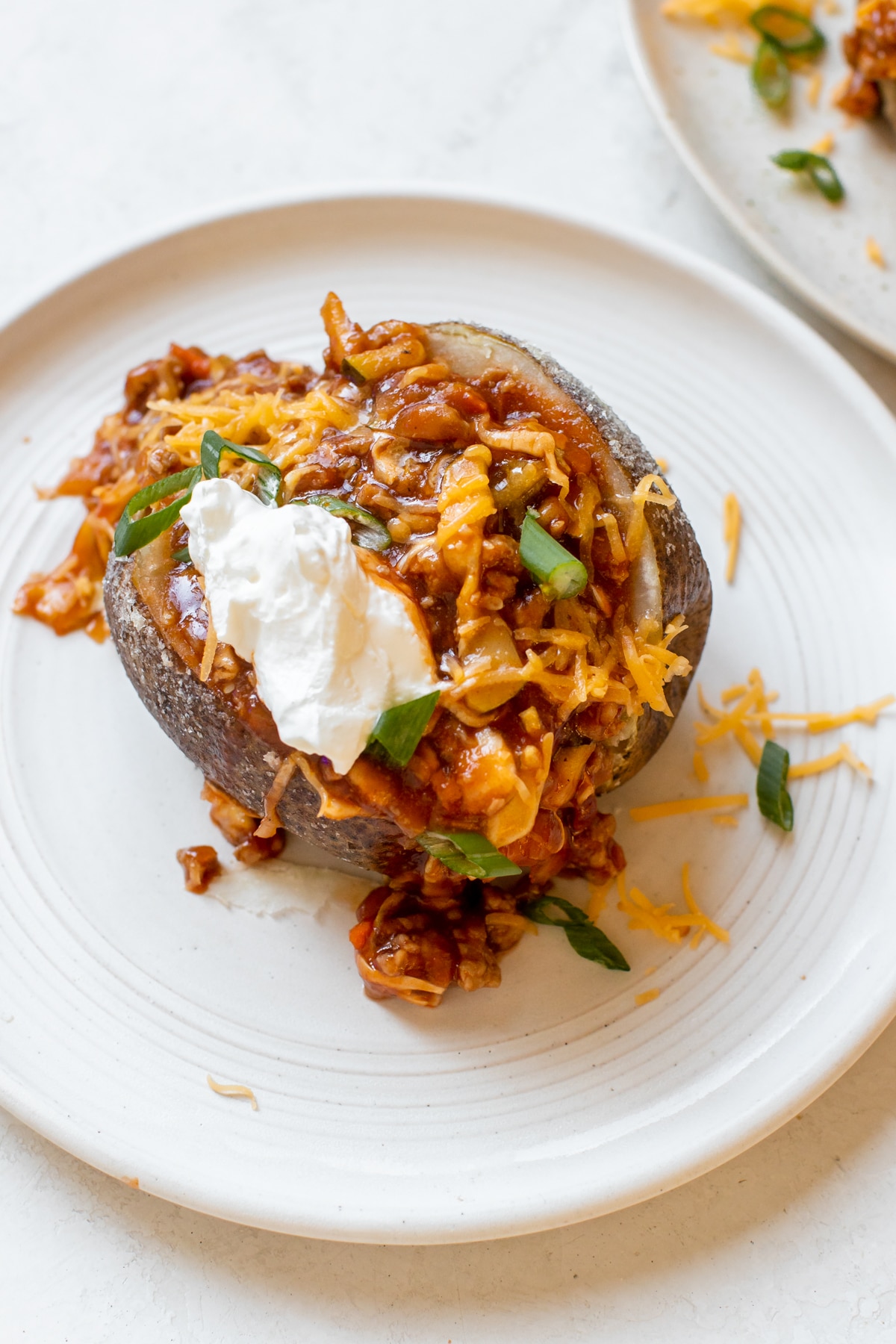a baked potato stuffed with a ground turkey meat sauce and topped with cheese, green onions and sour cream
