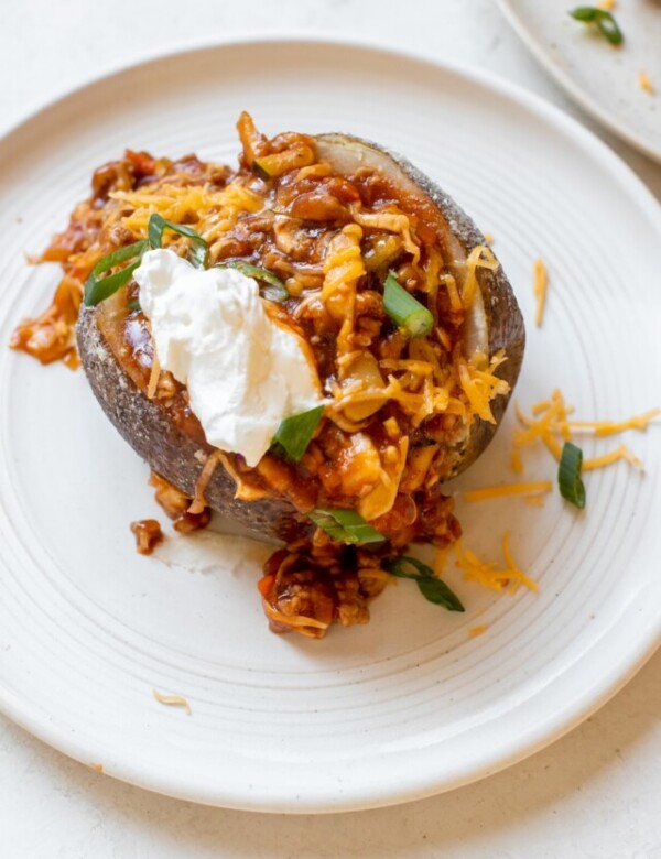 a baked potato filled with sloppy joe meat sauce and garnished with green onions, cheese and sour cream