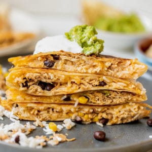 chipotle chicken quesadilla cut in half and stacked on top of each other topped with sour cream and guacamole