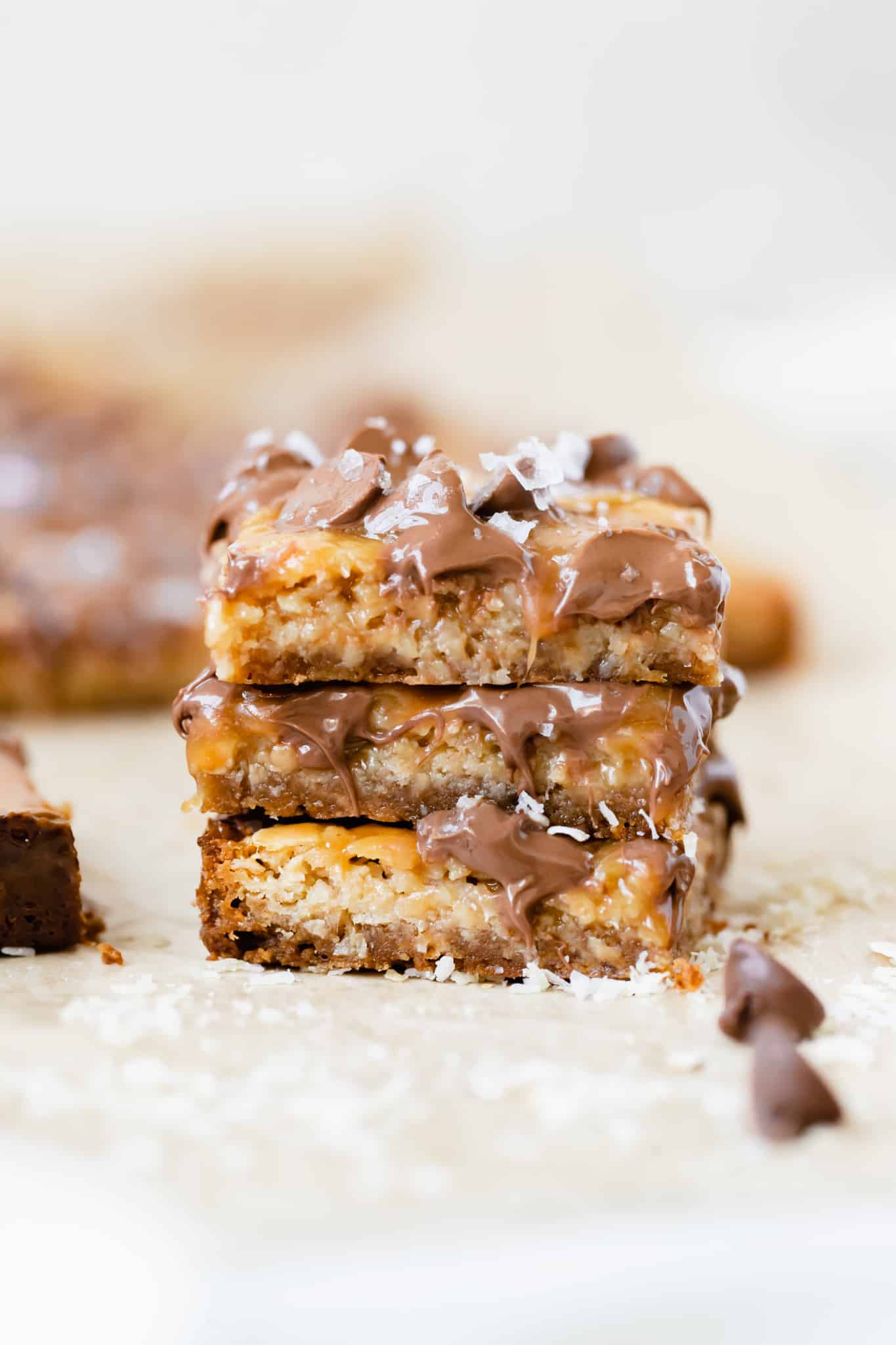 a stack of caramel chocolate bars topped with flaky sea salt on parchment paper