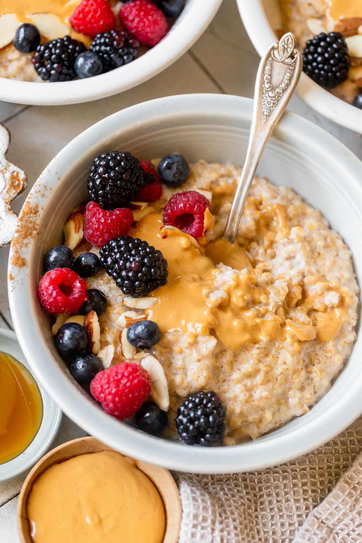 steel cut oatmeal in white bowls topped with peanut butter and fresh berries. 