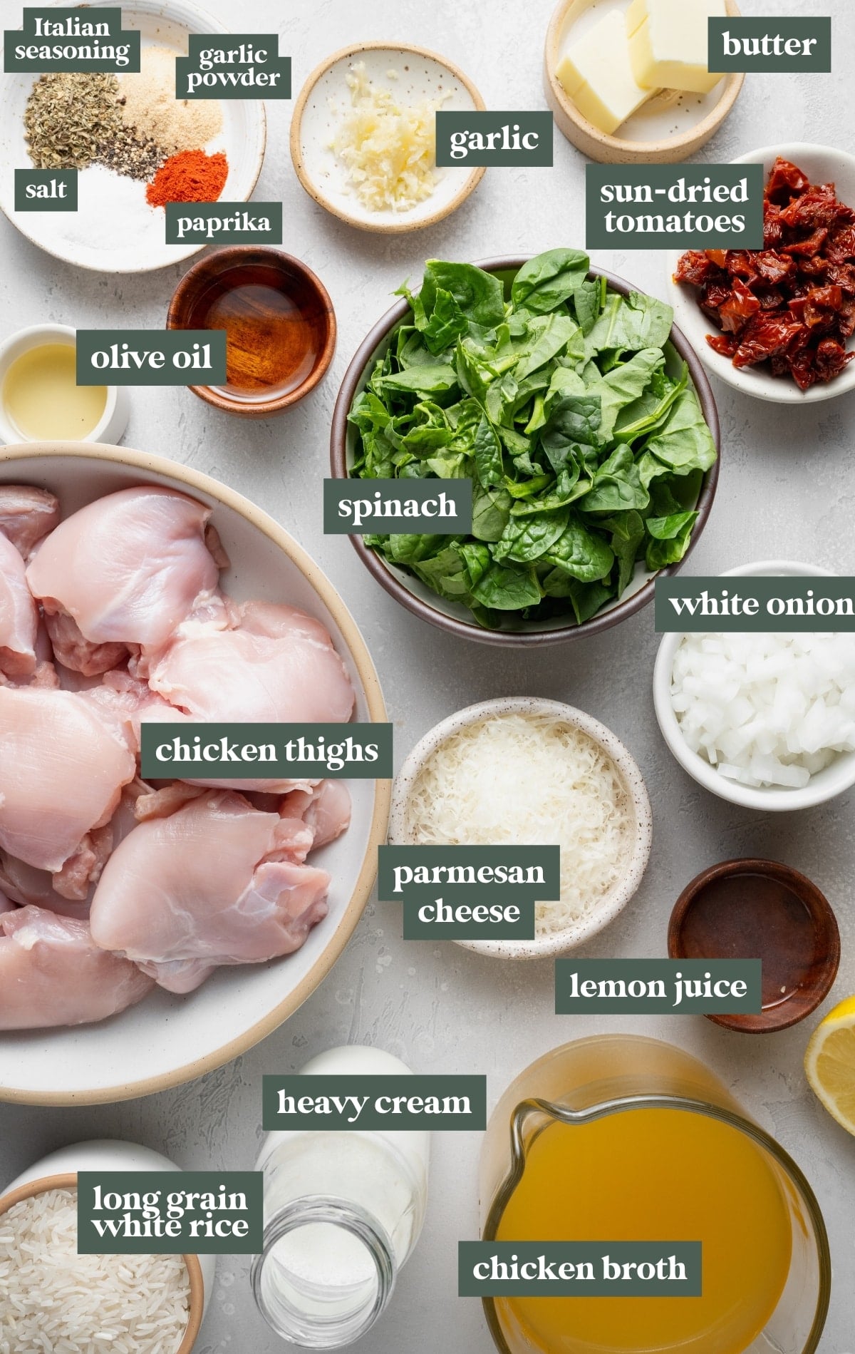 Ingredients for creamy Tuscan chicken and rice arranged on a countertop, including chicken thighs, long-grain white rice, chicken broth, heavy cream, Parmesan cheese, spinach, white onion, garlic, sun-dried tomatoes, butter, olive oil, lemon juice, Italian seasoning, paprika, garlic powder, and salt.