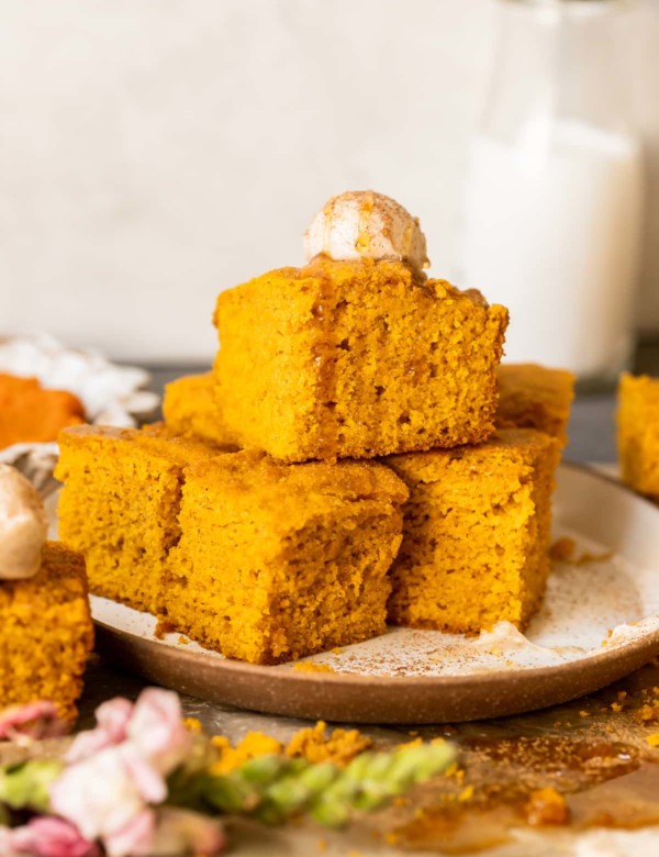 squares of pumpkin cornbread stacked on a tan plate and topped with a scoop of butter and a drizzle of honey