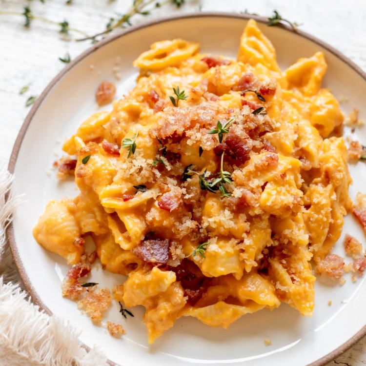 macaroni pasta on a white plate in a pumpkin cheddar cheese sauce garnished with bacon and fresh thyme.
