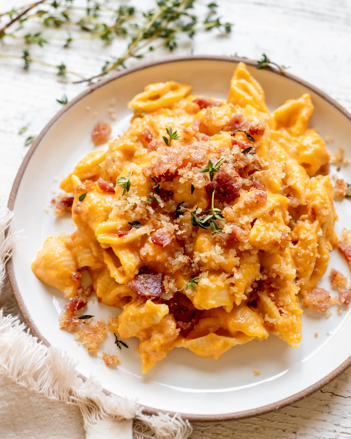 macaroni pasta on a white plate in a pumpkin cheddar cheese sauce garnished with bacon and fresh thyme. 