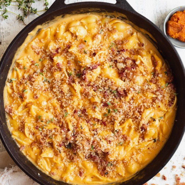 macaroni pasta on in a black cast iron skillet in a pumpkin cheddar cheese sauce garnished with bacon and fresh thyme.