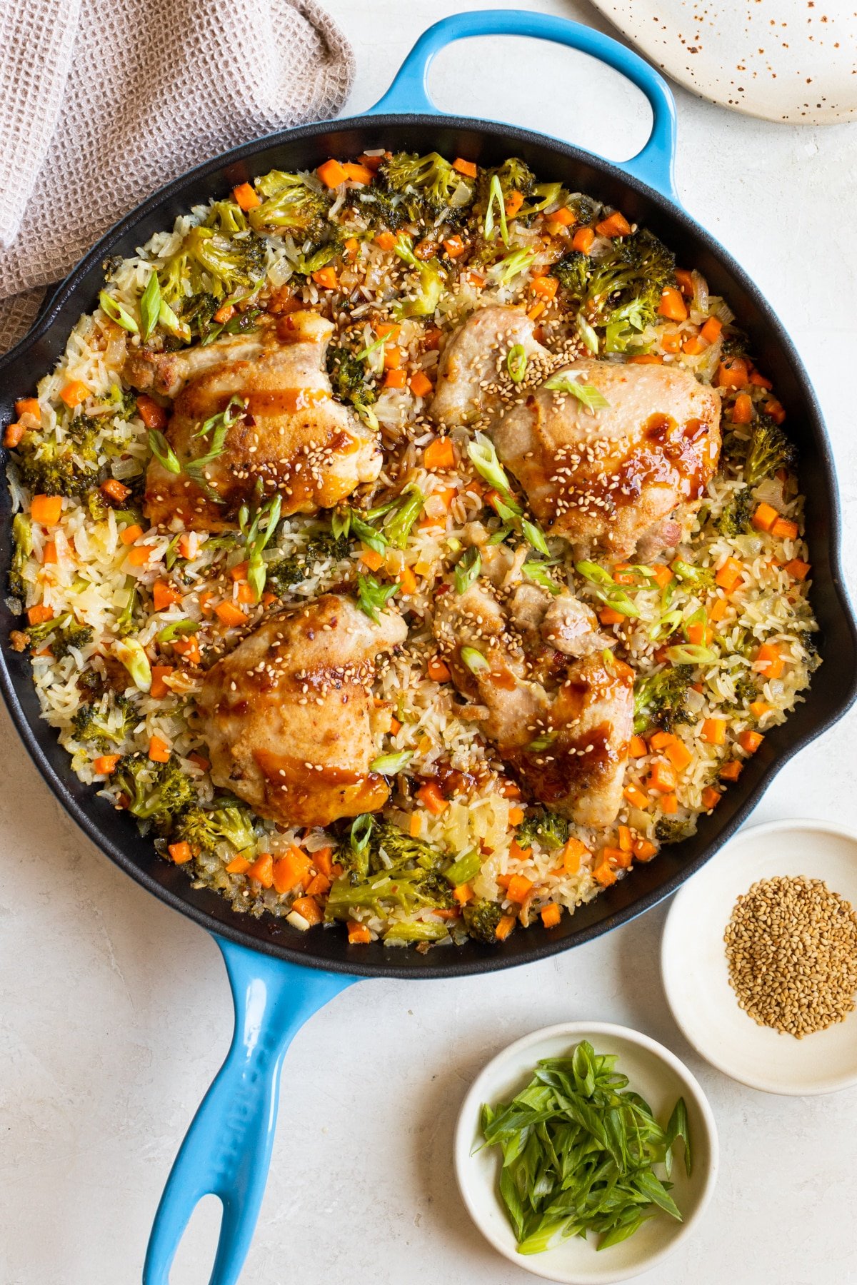 chicken and rice with teriyaki sauce, sesame seeds and green onions on top in a blue cast iron skillet. 