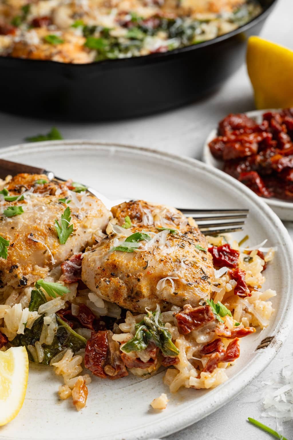 Close-up of a plated serving of creamy Tuscan chicken and rice with browned chicken thighs, creamy Parmesan rice, spinach, sun-dried tomatoes, grated Parmesan, fresh parsley, and a lemon wedge.